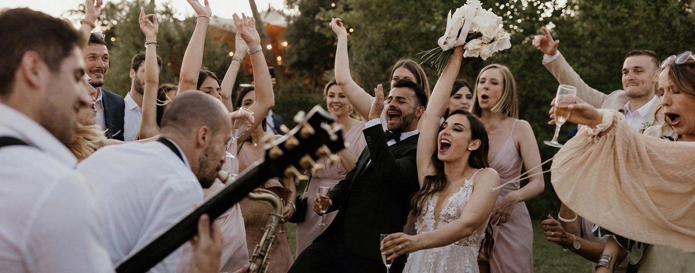 Guitarist playing for a crowd of smiling guests at an outdoor party.